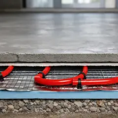 Warstwa betonu z czerwonymi rurkami ogrzewania podłogowego. To kluczowy etap wygrzewania posadzki po roku, zapewniający jej trwałość i komfort.