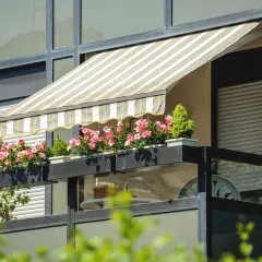 Pasiasty daszek na balkon w bloku chroni przed słońcem kwitnące różowe kwiaty w skrzynkach.