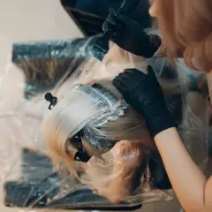 Fryzjerka nakłada farbę na blond włosy. Zastanawiasz się, ile trzymać farbę na włosach? Czas zależy od efektu.
