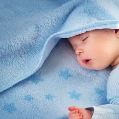 Sover gott under ett mjukt, blått täcke med stjärnor. Liten bebis svettas lite i sömnen.