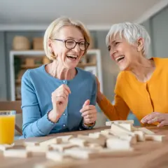 Deux femmes âgées rient en jouant au Jenga, une activité maison de retraite pleine de joie et de complicité.