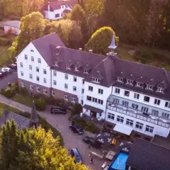 Luftaufnahme des Klosters Ommerborn mit seinem markanten Turm, umgeben von Bäumen und einem Poolbereich.