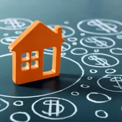 Casa naranja sobre fondo oscuro con símbolos de dólar dibujados. BBVA tasación de inmuebles.