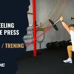 Mężczyzna w pozycji wykrocznej wykonuje ćwiczenie half kneeling landmine press.