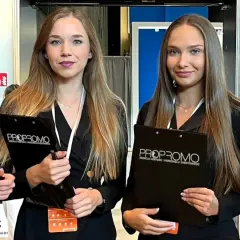 Dwie uśmiechnięte hostessa z agencji PROPROMO trzymają teczki z logo firmy.
