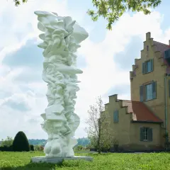 Weiße, organische Skulptur vor einem gelben Gebäude im Freien.