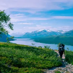 Vandra i Norrland med storslagen utsikt över sjö och snöklädda berg. En ensam vandrare med ryggsäck går på en stenstig.