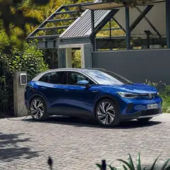 Niebieski VW ID.4 ładuje się przy nowoczesnym domu. Elektryczny SUV stoi na podjeździe, podłączony do ładowarki.