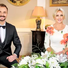 Mężczyzna w garniturze i kobieta w sukience w kwiaty siedzą obok siebie.