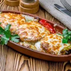 Kotlet po góralsku zapieczony z serem i warzywami w glinianym naczyniu, udekorowany natką pietruszki.