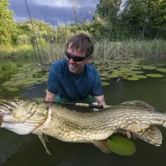 Szczęśliwy wędkarz trzyma w wodzie ogromnego szczupaka, być może największego szczupaka na świecie.