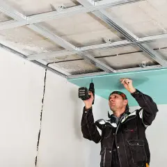 Un ouvrier installe une plaque de plâtre sur une structure métallique, créant ainsi un plafond technique.