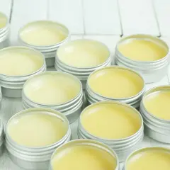 Piccoli barattoli argentati pieni di balsamo giallo, un prodotto naturale a base di cera d'api, pronti per essere usati.