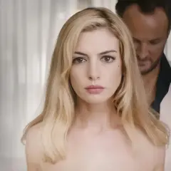 Anne Hathaway, protagonista de "L'isola dell'inganno", con uno sguardo intenso. Dietro di lei, un uomo in giacca bianca.