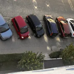 Szary samochód, czerwony, czarny, granatowy, rudy, biały, ciemnogranatowy i srebrny stoją na parkingu. Może to być inspiracja do wypełnienia wniosku o miejsce parkingowe wzór.