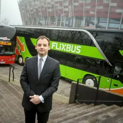 Mężczyzna w garniturze stoi przed zielonym autokarem Flixbus i czerwonym autokarem Polskibus.