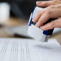 Dłoń z pieczątką nad dokumentami, które mogą być pozwolenie na budowę.