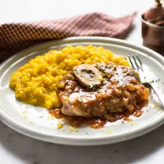 Un piatto di ossobuco ricetta originale con risotto giallo zafferano, guarnito con prezzemolo e scorza di limone.