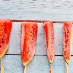 Vier Wassermelonenstücke auf Stäbchen, bereit zum Wassermelone einfrieren. Perfekt für heiße Sommertage.
