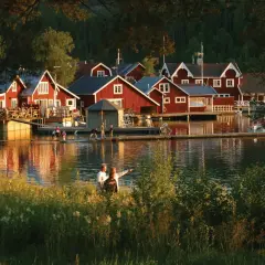 Solnedgång över Norrfjällsviken med röda sjöbodar och folk som njuter av kvällen vid vattnet.