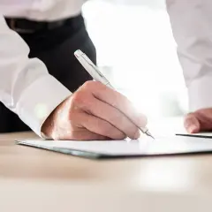 Mężczyzna w białej koszuli podpisuje dokument. Dowiedz się, jak sprawdzić, kto jest właścicielem mieszkania w bloku.