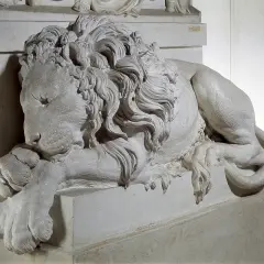 Leone scolpito, simbolo di forza, riposa ai piedi della tomba di Clemente XIII. La sua criniera fluente e le zampe possenti trasmettono un senso di maestà e quiete eterna.