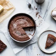 Una torta tenerina al cioccolato, appena sfornata, con ingredienti come burro, uova e cioccolato disposti attorno.