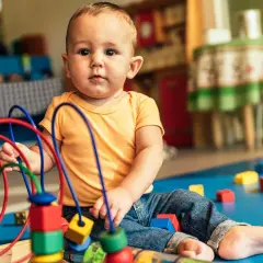 Maluch bawi się kolorowymi, drewnianymi zabawkami stymulującymi rozwój dziecka. W tle widać inne klocki i meble.
