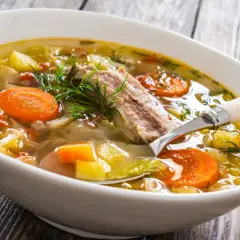 Aromaticzna zupa na żeberkach z warzywami i koperkiem, podana w białej misce na drewnianym stole.