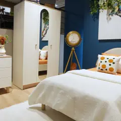 Ein gemütliches boho style jugendzimmer mit weißem Bett, Kleiderschrank und Kommode. Ein buntes Chamäleon-Bild ziert die Wand.