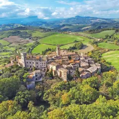 Un borgo toscano arroccato su una collina, circondato da dolci colline verdi e campi coltivati. Un esempio dei borghi toscani più belli.