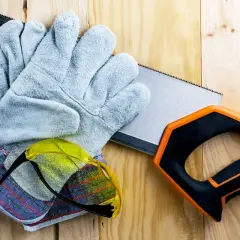 Guantes anticorte niveles, gafas de seguridad y sierra de mano sobre madera.