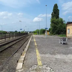 Pusta stacja kolejowa Opoczno Kielce. Torowisko, peron z ławką i żółtą linią, budynek dworca.