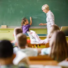 Eine Lehrerin steht vor einer Tafel, während ein Kind schreibt. Es ist schön, Lehrer zu sein und Wissen zu vermitteln.