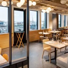 Restaurant moderne avec vue sur Paris. Tables dressées, lumières douces, et le logo "Printemps du Goût" visible.