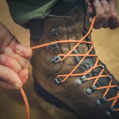 Hände binden orange Schnürsenkel an braunen Wanderschuhen. Bereit für das nächste Abenteuer.