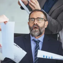 Zaskoczony mężczyzna w okularach, otoczony przez współpracowników z dokumentami. Czy można mieć dwie umowy o pracę?
