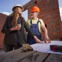 Architektka i budowlaniec omawiają plany. Dyskutują, ile trwa pozwolenie na budowę, podczas gdy budowa trwa.