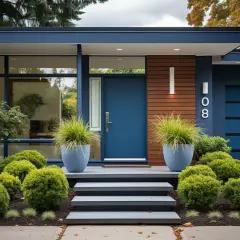 Niebieskie drzwi wejściowe domu z nowoczesną architekturą, otoczone bujną zielenią i ozdobnymi donicami.