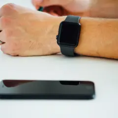 Czarny smartwatch na nadgarstku, obok leży wyłączony smartfon. Co zrobić, gdy smartwatch nie chce się włączyć?