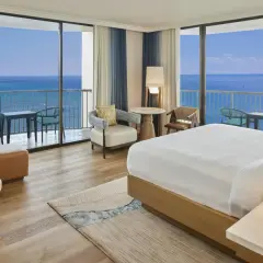 Pokój hotelowy z widokiem na ocean, idealny na wakacje hawaje all inclusive. Wygodne łóżko, sofa i balkon z stolikiem.