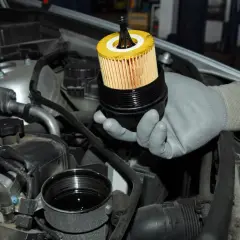Mano guantata mostra il filtro olio motore appena estratto dal suo alloggiamento, pronto per la sostituzione.