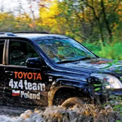Czarny Toyota Land Cruiser 100 z napisem "4x4 team Poland" pokonuje błotnistą trasę w lesie.