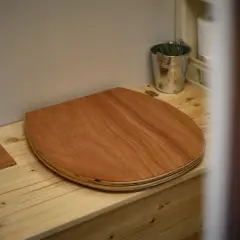 Un siège en bois pour toilettes sèches de camping-car, avec un petit seau de plantes et du papier toilette à proximité.