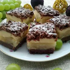 Szybkie ciasto z gruszkami i budyniem, posypane cukrem pudrem, na talerzu z winogronami.
