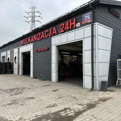 Budynek wulkanizacji z napisem "Wulkanizacja 24H", stosy opon i otwarte bramy garażowe.