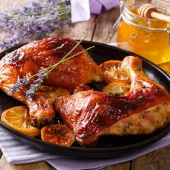 Muslos de pollo al horno dorados y jugosos, servidos con rodajas de limón y un toque de lavanda. Un tarro de miel dorada acompaña este delicioso plato.