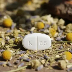 Biała tabletka z oznaczeniem "K 0.5" leży wśród suszonych kwiatów rumianku i lawendy. To może być clonazepam, lek na uspokojenie.