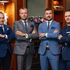 Czterech mężczyzn w garniturach stoi z założonymi rękami.