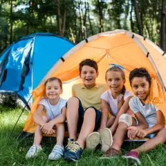 Niños sonríen en una tienda de campaña naranja, disfrutando de una acampada libre en Cantabria.